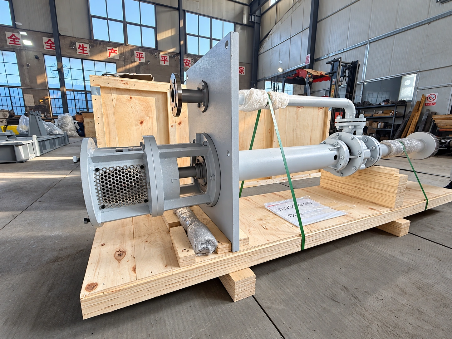 Bơm cột dài màu xám và đường ống trên pallet trong xưởng.